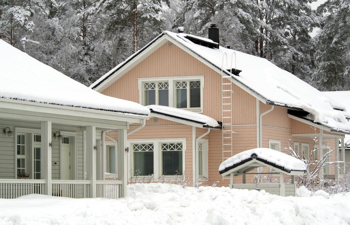 Omakotitaloja talvella, lunta on kerääntynyt talojen katoille ja pihamaille.